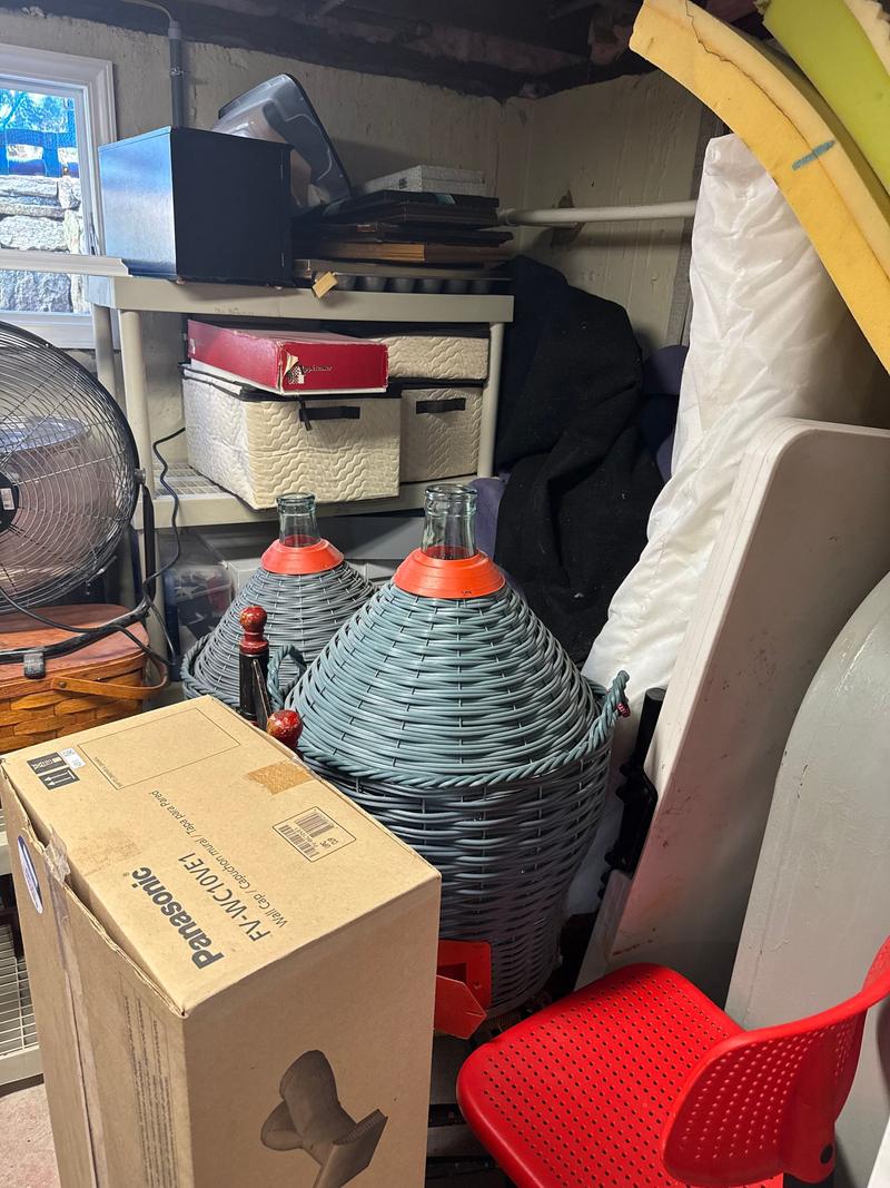 Crowded storage area packed with boxes, bottles, a fan and household items before a clean-out
